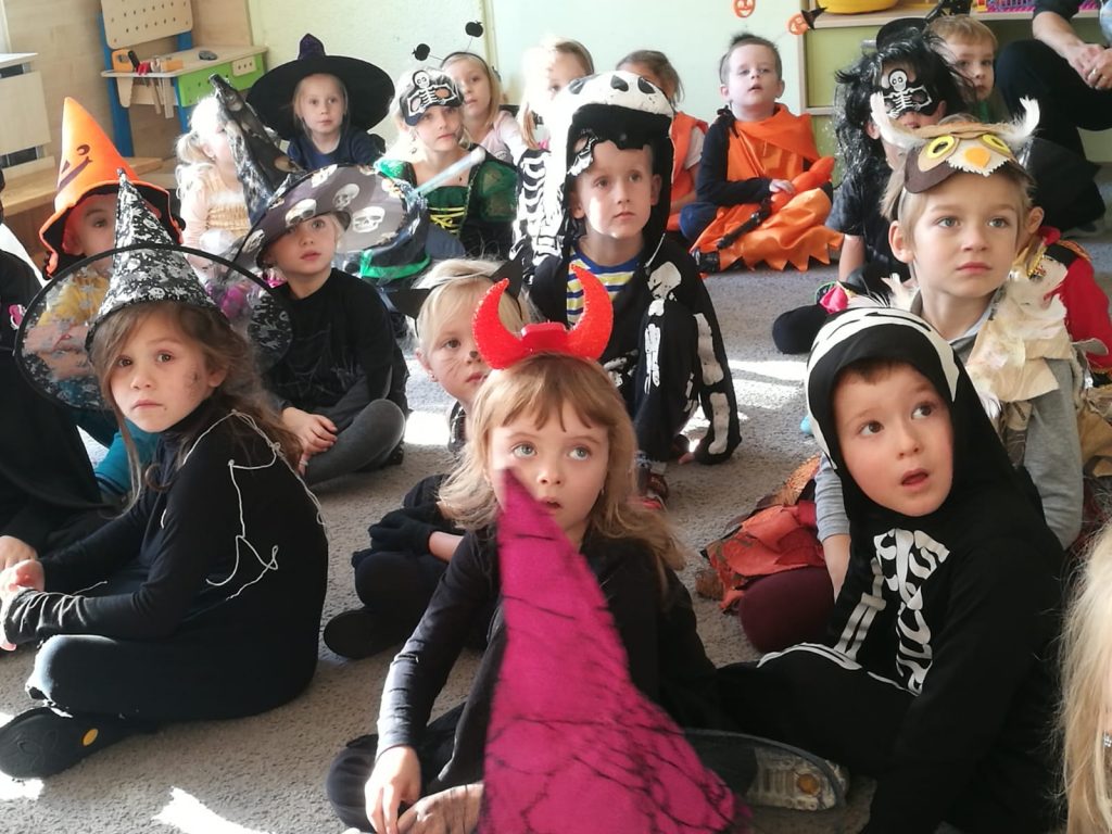 Děti sedí v kostýmech a poslouchají.