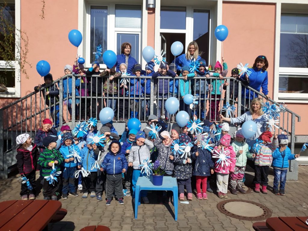 Děti stojí před školkou a jsou oblečeny do modrého oblečení.