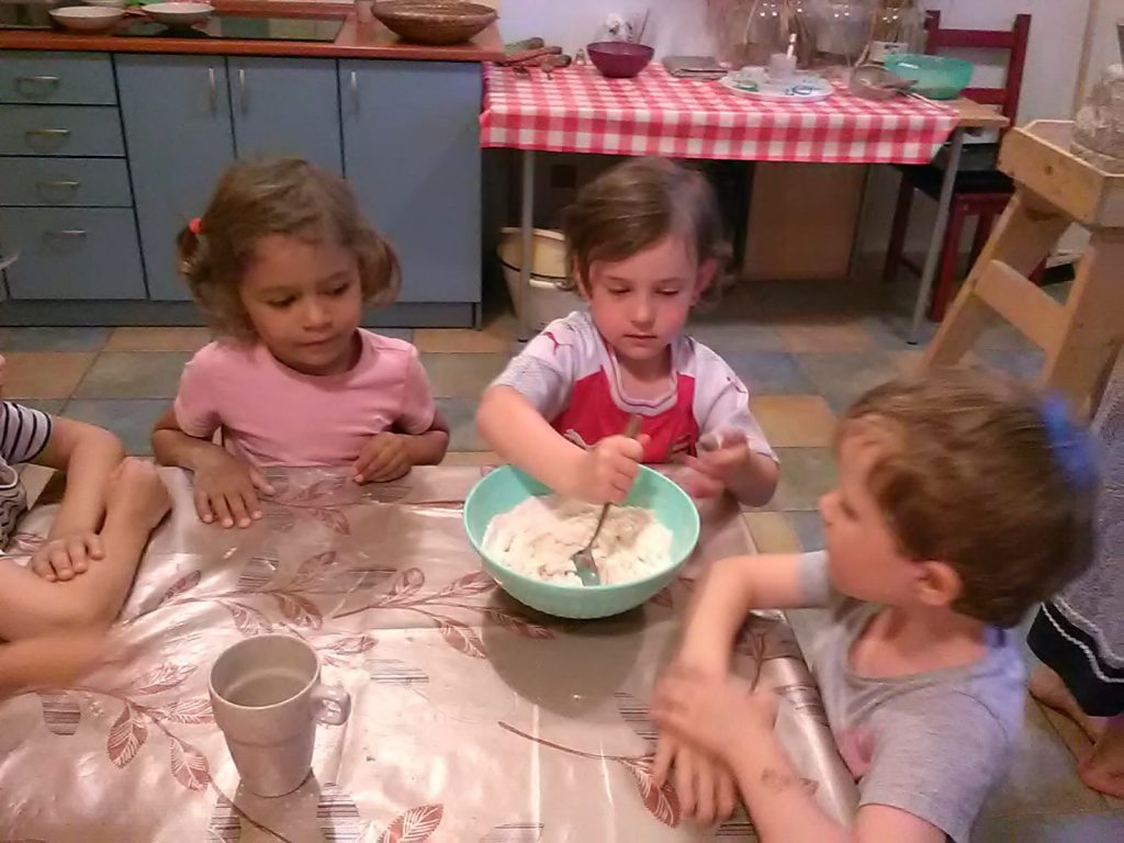 Děti sedí u stolu a holčička míchá těsto.