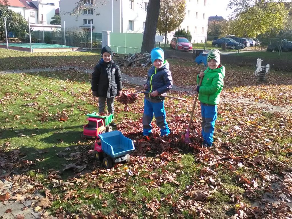 Děti hrabou listí na zahradě.
