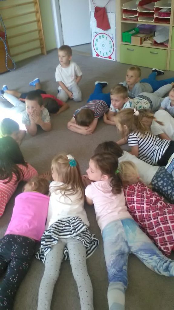Děti leží v kruhu na koberci.