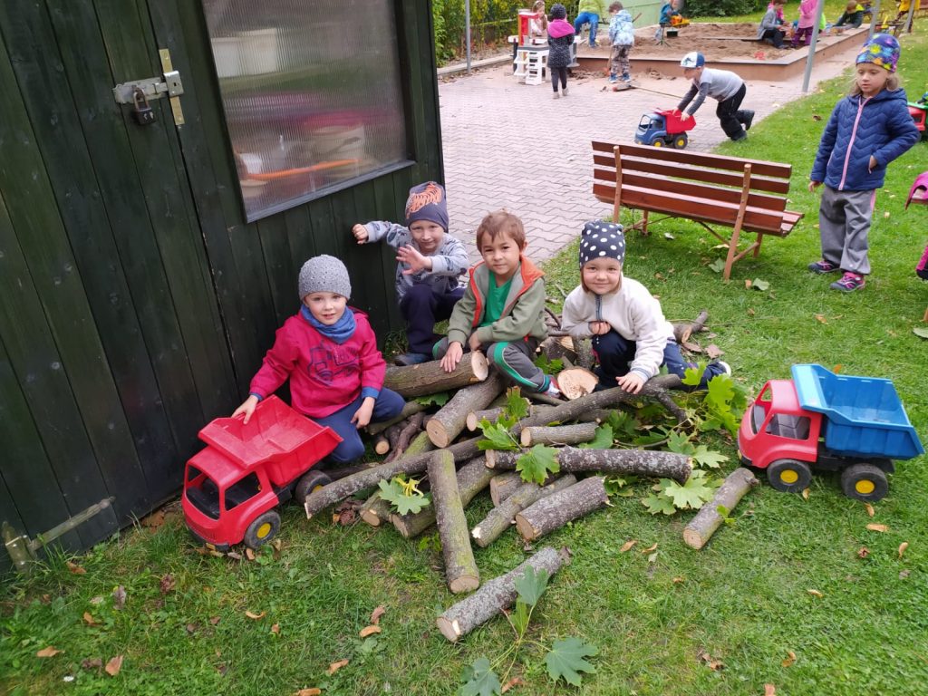 Děti si hrají na zahradě školky se dřevem.