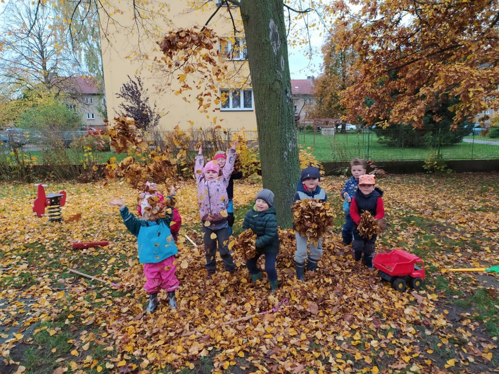 Děti hází listí na zahradě školky.